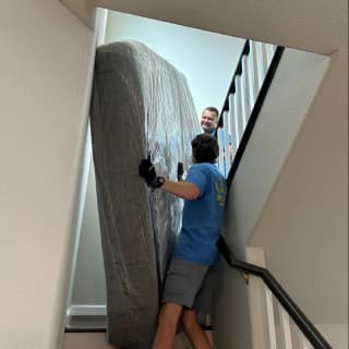 A team of movers carefully navigating a large wrapped item through a tight stairway.