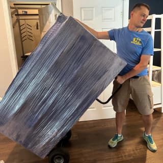 A smiley mover using a hand truck to transport a large, wrapped piece of furniture, showcasing experienced handling.