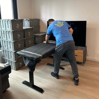 A moving specialist carefully wrapping a large desk inside a modern apartment, showcasing expert handling in a residential moving service.