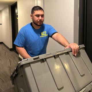 A concentrated mover carries a stack of large storage bins across a hallway, demonstrating careful handling during a residential relocation.