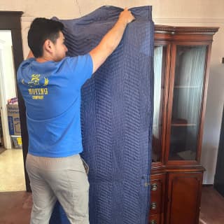 A careful mover wrapping a large wooden cabinet with a protective blanket, demonstrating expert handling.