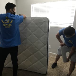 A team of two movers in a bedroom busy protecting a mattress with multiple layers of shrink wrap. Great job preparing items for local and long-distance moving.