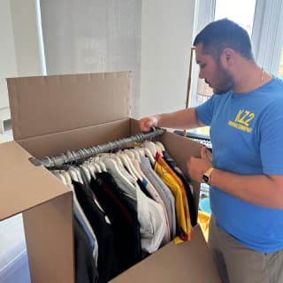 Experienced mover neatly packing clothes into a wardrobe box, ensuring careful organization for the move.