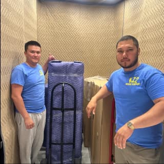 A team of experienced movers carefully transporting large, wrapped furniture into an elevator.