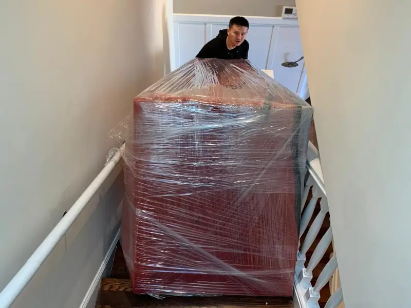 KZ2 movers taking a wrapped couch through a narrow staircase